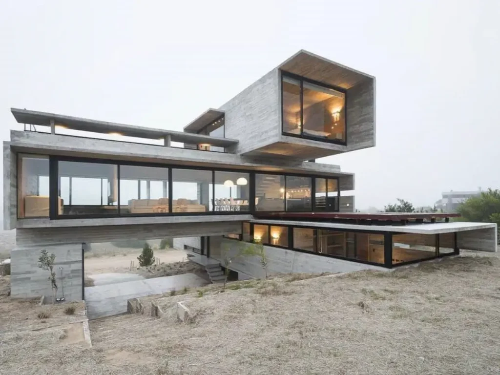 A multi-level brutalist house built like a bridge over a hillside, with a dramatic cantilevered top floor and expansive glass walls.