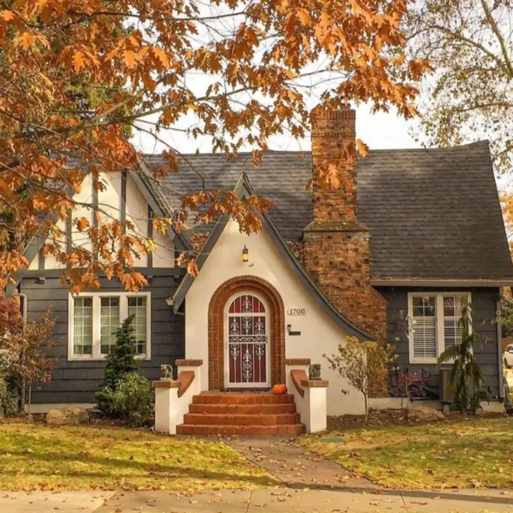 A country house design with Tudor-style details, including a white stucco arched entryway and a large brick chimney.