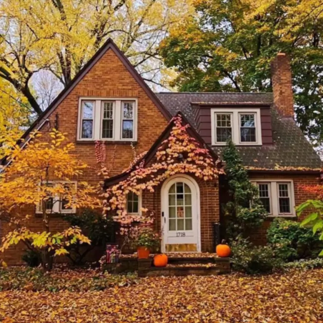 A charming brick country house design with an arched front door and climbing vines, set in a beautiful autumn landscape.