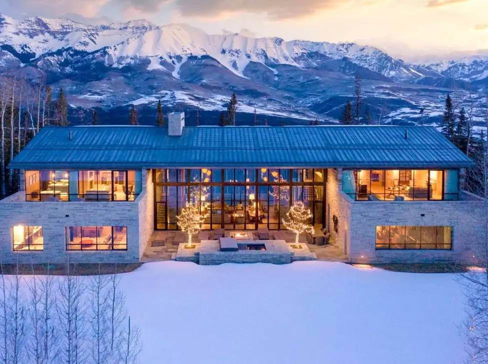 16 Mountain Mansions That Define Luxury Alpine Living 13 Symmetrical modern mountain mansion designed as a glass pavilion, perfectly framing a cinematic view of a snow-capped mountain range.