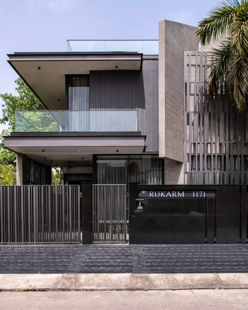 A modern concrete and dark-clad home featuring a glass balcony and vertical privacy screens.