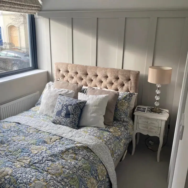 A small cozy bedroom featuring a beige tufted headboard set against a gray board and batten wall with a patterned blue and yellow quilt.