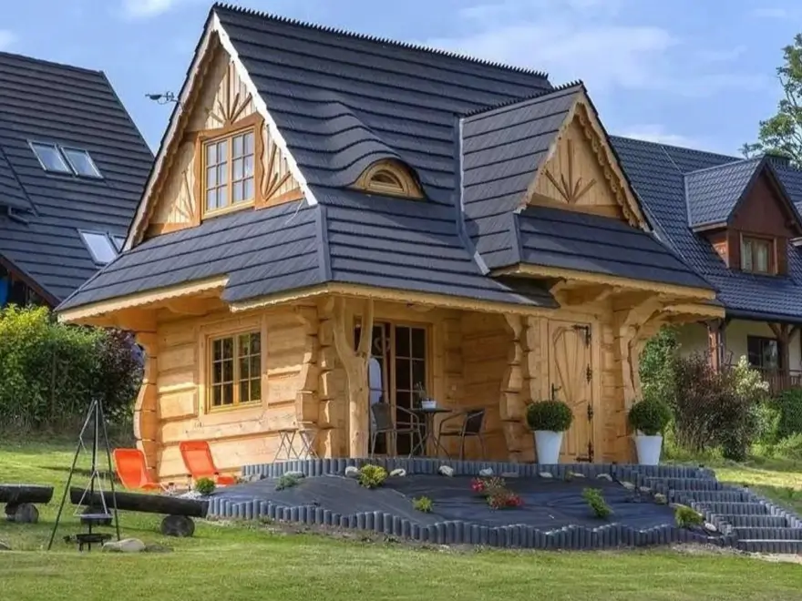 60 Charming Small Log Cabin Ideas to Inspire Your Rustic Retreat 11 A small log cabin with a unique, ornate dark gray roof and light-colored logs, set on a grassy hill.