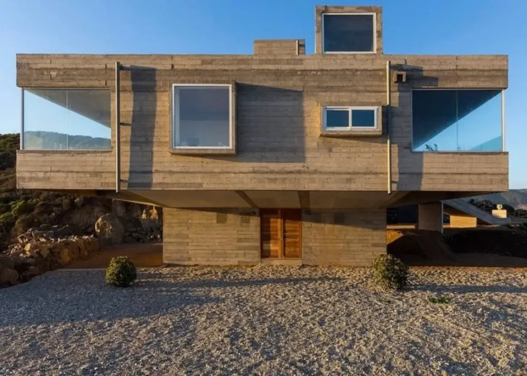 A powerful brutalist house design featuring a top-heavy composition, with a massive cantilevered concrete upper level poised over a smaller, recessed ground floor.
