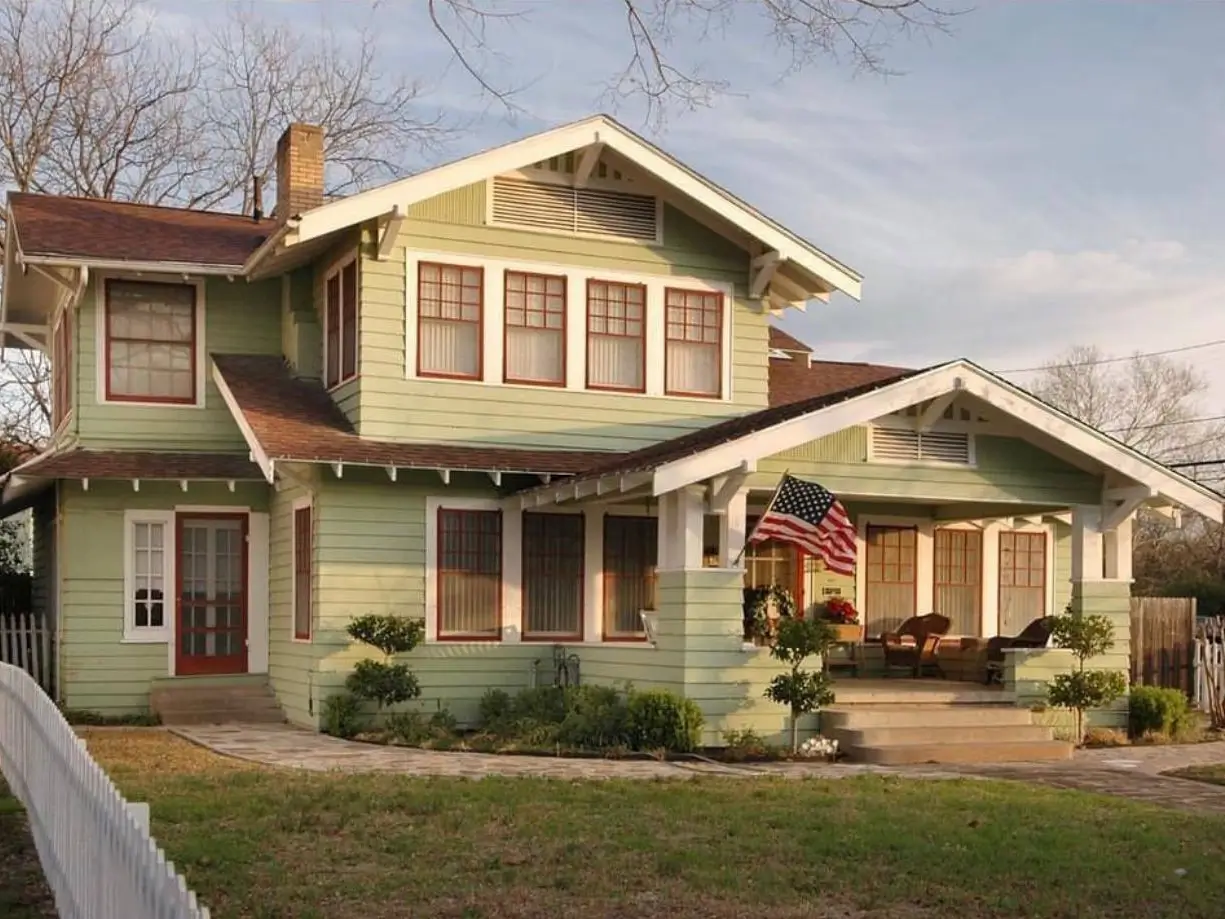 A classic American craftsman house with light green siding, contrasting red window trim, and a wide, welcoming front porch.