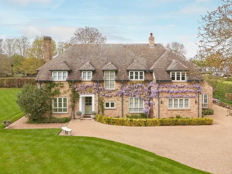 A large brick British country house showcasing classic English country home design with purple wisteria, a gravel driveway, and a manicured lawn.