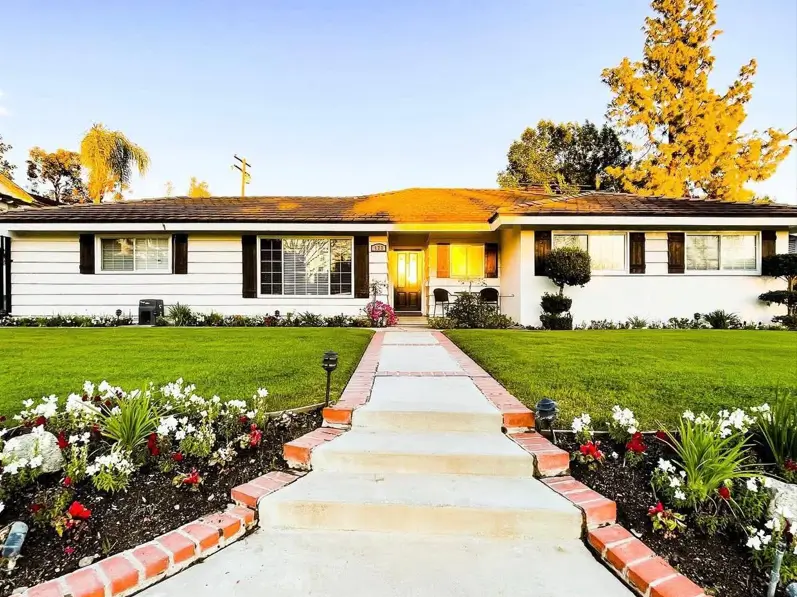 A classic white ranch house with dark shutters and a welcoming walkway at sunset, showcasing timeless exterior design ideas.
