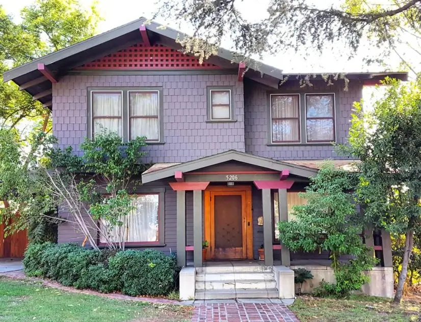 A craftsman house exterior with muted purple-gray shingles and vibrant red accents on the decorative lattice and porch.