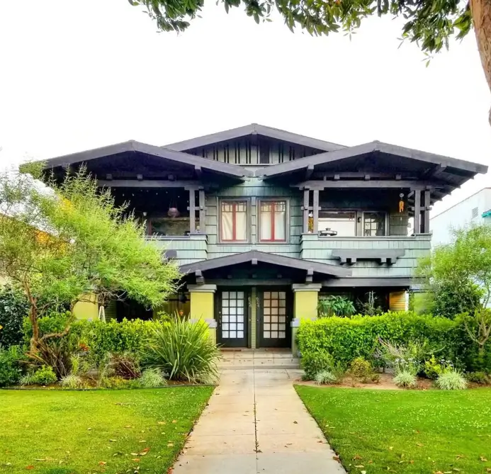 A large craftsman house exterior with dramatic low-pitched rooflines, deep eaves, and soft sage-green siding.