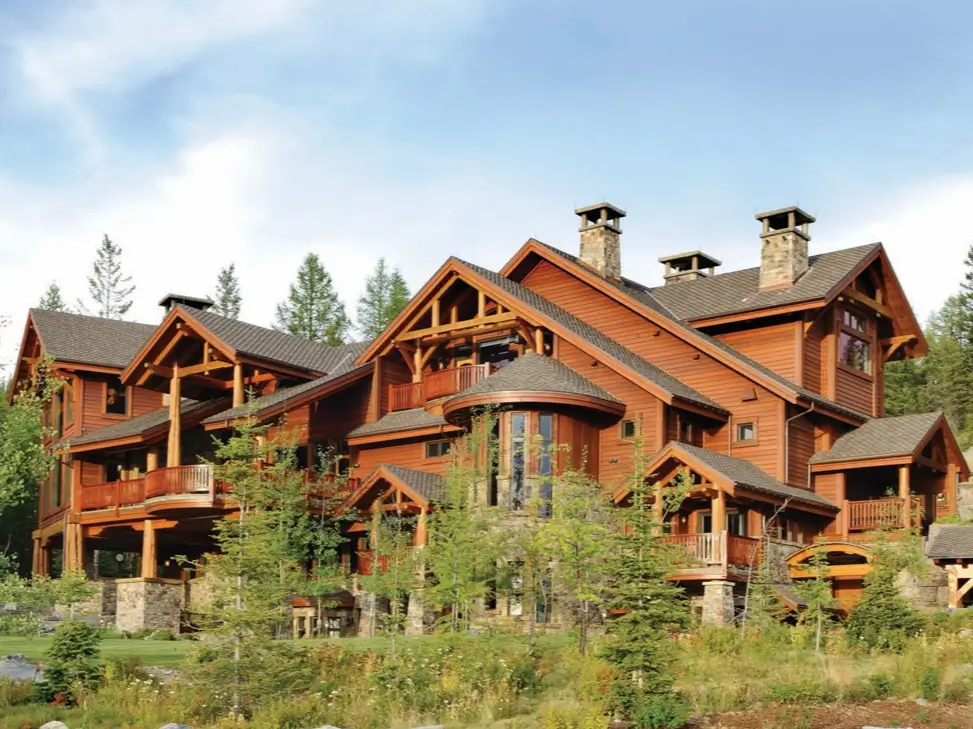 16 Mountain Mansions That Define Luxury Alpine Living 4 A grand timber-frame mountain mansion with intricate woodwork, multiple gables, and stone chimneys, set among young pine trees.