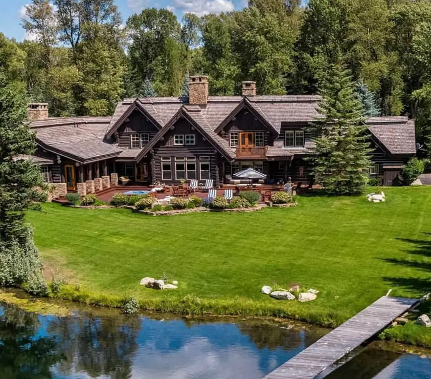 Embracing Grandeur: 25 Inspiring Ideas for Large Log Cabin Homes 3 An aerial view of a large, dark wood log cabin home with an expansive back patio and a lush green lawn leading to a private lake dock.