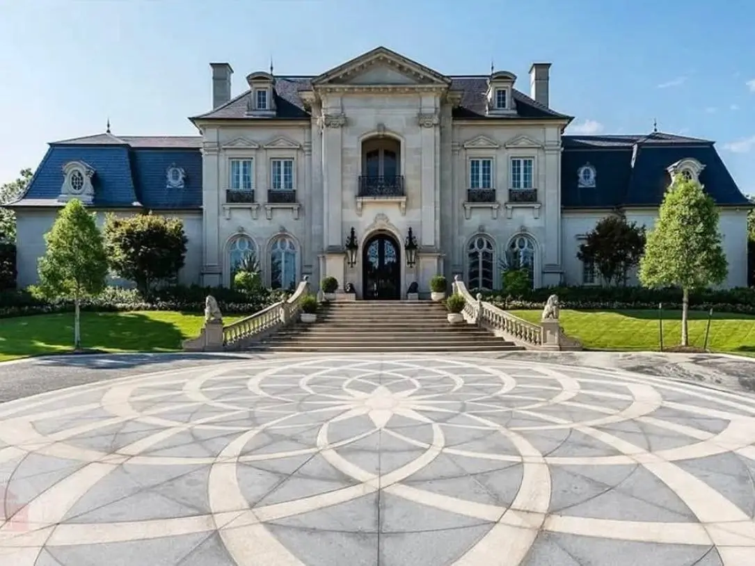 A grand luxury mansion with a sweeping stone staircase and an artfully patterned motor court.