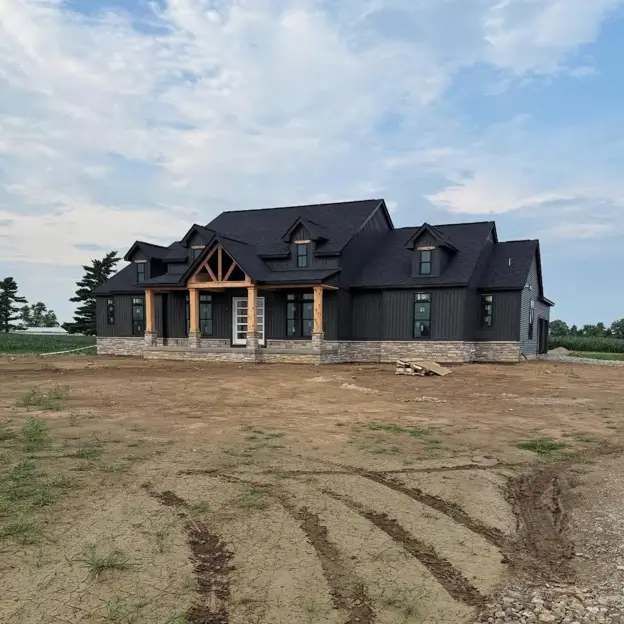 A striking modern black farmhouse with a timber-frame porch, vertical siding, and stone accents, showcasing a popular black house design.