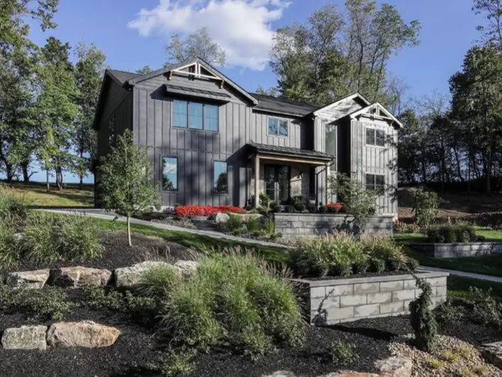 A stunning modern black house exterior with vertical siding, set within a tiered landscape of stone retaining walls, lush grasses, and dark mulch, representing a sophisticated black house design.