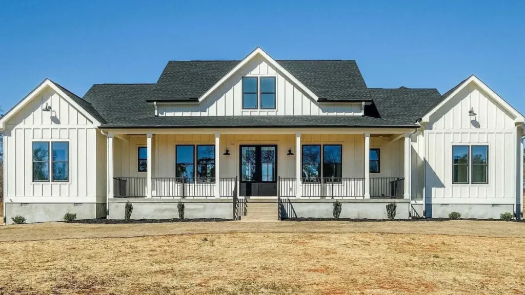 A symmetrical modern white farmhouse exterior with vertical siding, a dark shingle roof, and a welcoming front porch with a black double door.
