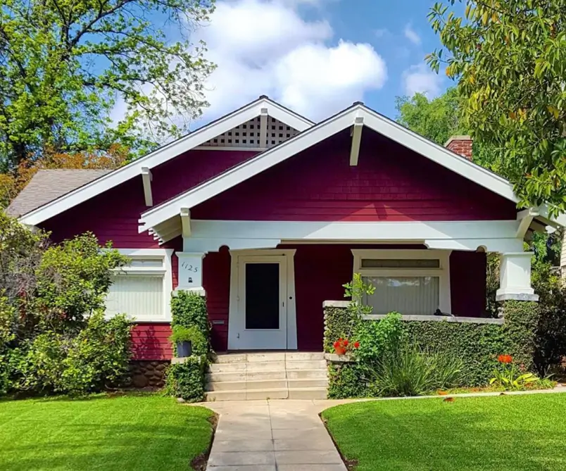 A classic craftsman bungalow with a rich burgundy siding exterior and sharply defined white trim on the roofline and porch.
