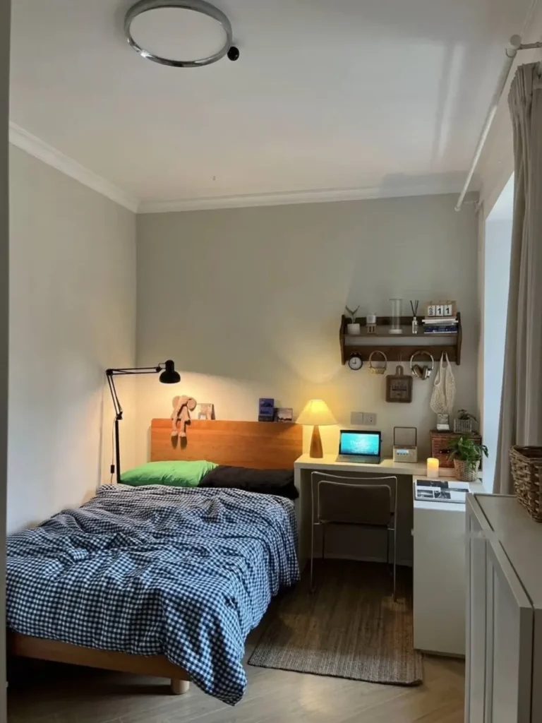 A small cozy bedroom with a wooden bed and integrated desk, featuring a blue gingham duvet and warm lighting for a calm, functional space.