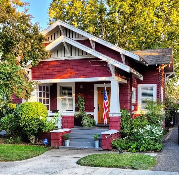 A vibrant red shingle craftsman bungalow with crisp white trim on the exposed rafters and porch columns.