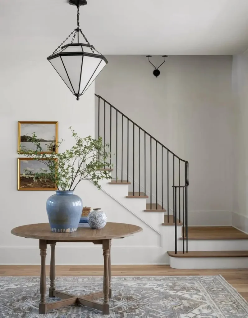Modern farmhouse entryway with a round wooden table, black metal staircase, and geometric pendant light.