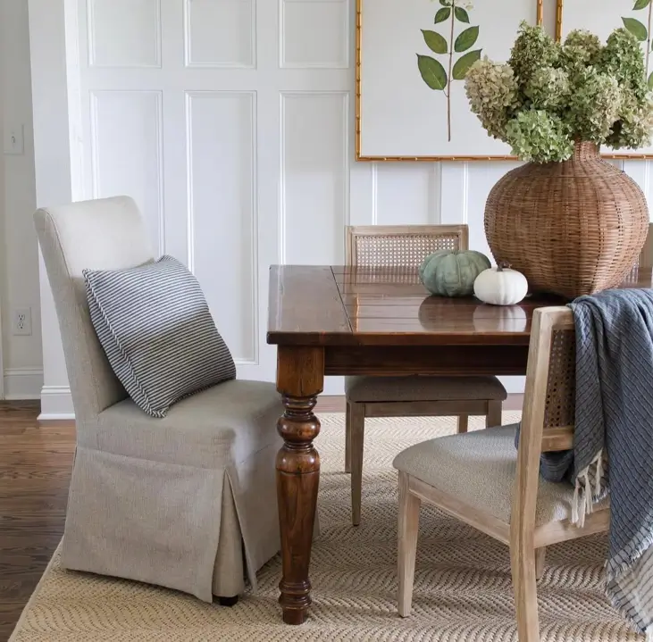 Modern farmhouse dining area with a wood table, mixed seating including a slipcovered chair, and white wall paneling.