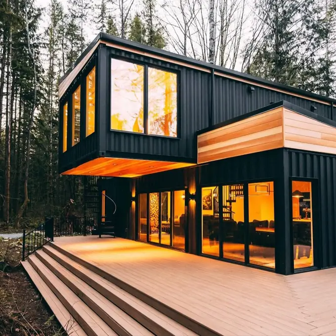 A stunning house design crafted from five black shipping containers, with a cantilevered upper level and wood accents, nestled in a forest.