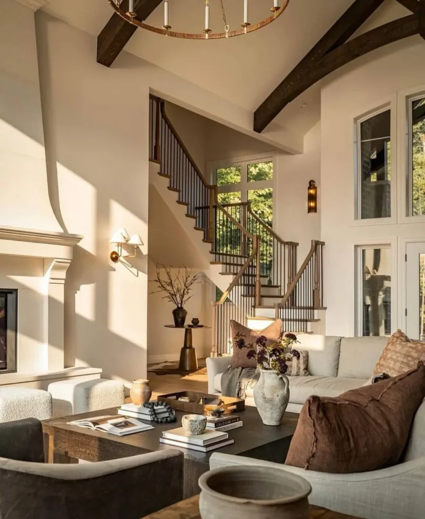 Modern farmhouse living room with high ceilings, dark wood beams, and a large curved white fireplace.