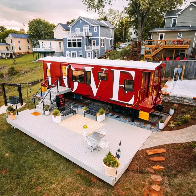 A unique house design featuring a red train caboose with "LOVE" painted on the side, connected to a modern deck.
