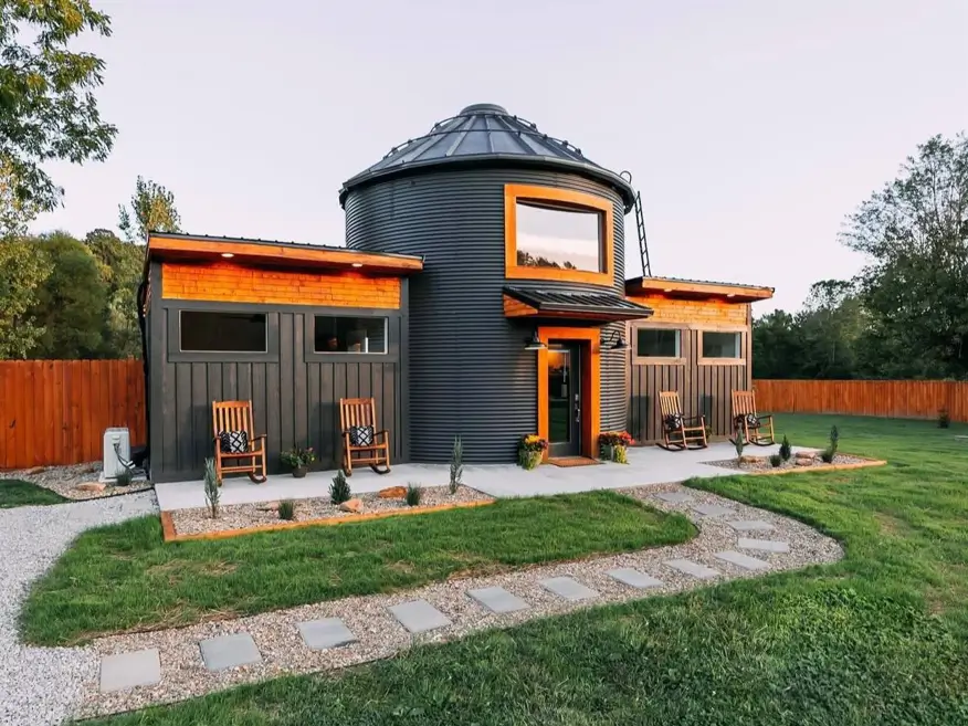 A unique house design featuring a converted black grain silo connected to modern wings with wood accents.