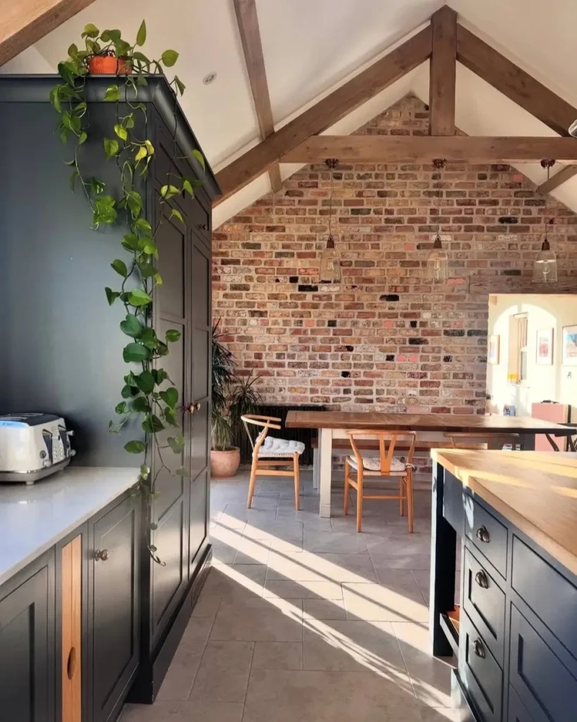 Modern farmhouse dining area with an exposed brick wall, vaulted ceiling with wood beams, and dark kitchen cabinets.