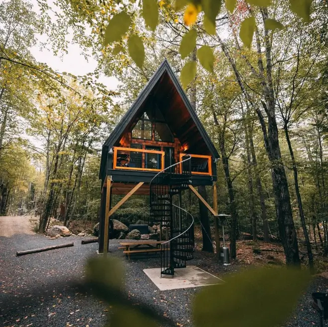 A beautiful modern house design of an elevated black A-frame cabin with a prominent spiral staircase in a forest setting.