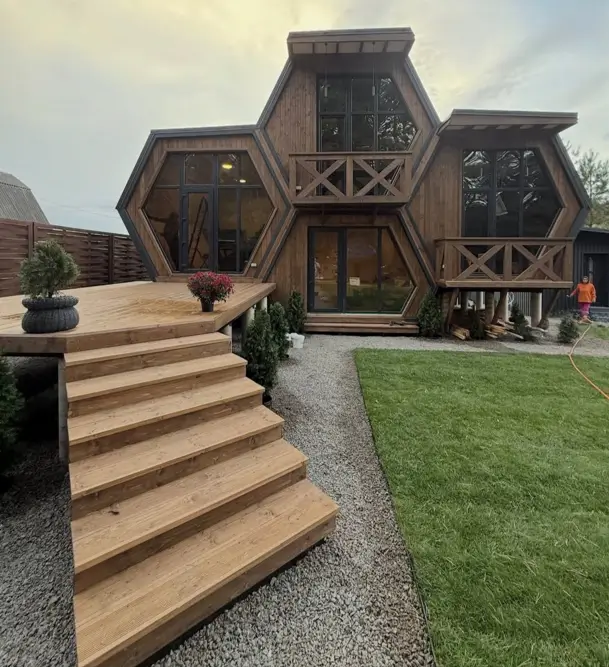 A unique house design with a wooden honeycomb structure, large hexagonal windows, and a spacious deck.
