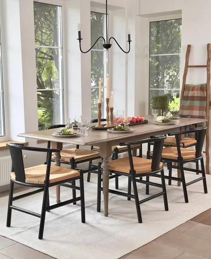 Modern farmhouse dining room with black and natural woven chairs around a light wood table under a simple black chandelier.
