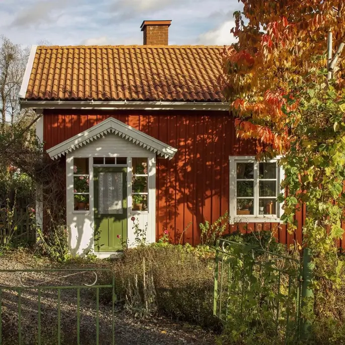A stunning house design of a traditional red cottage with a green door and tile roof in an autumn garden.