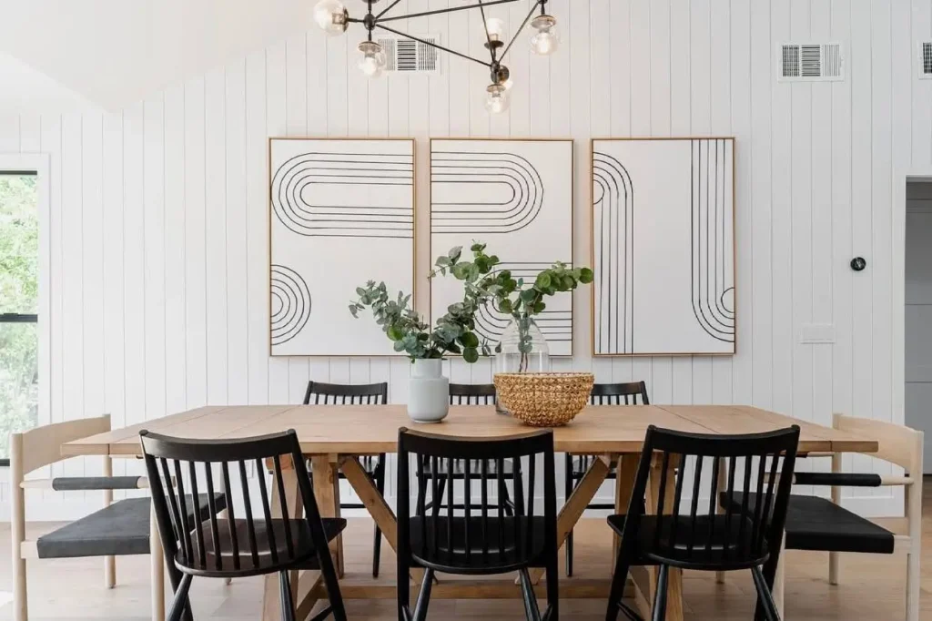 Modern farmhouse dining room with black spindle chairs, a wood table, and large graphic wall art against a white paneled wall.