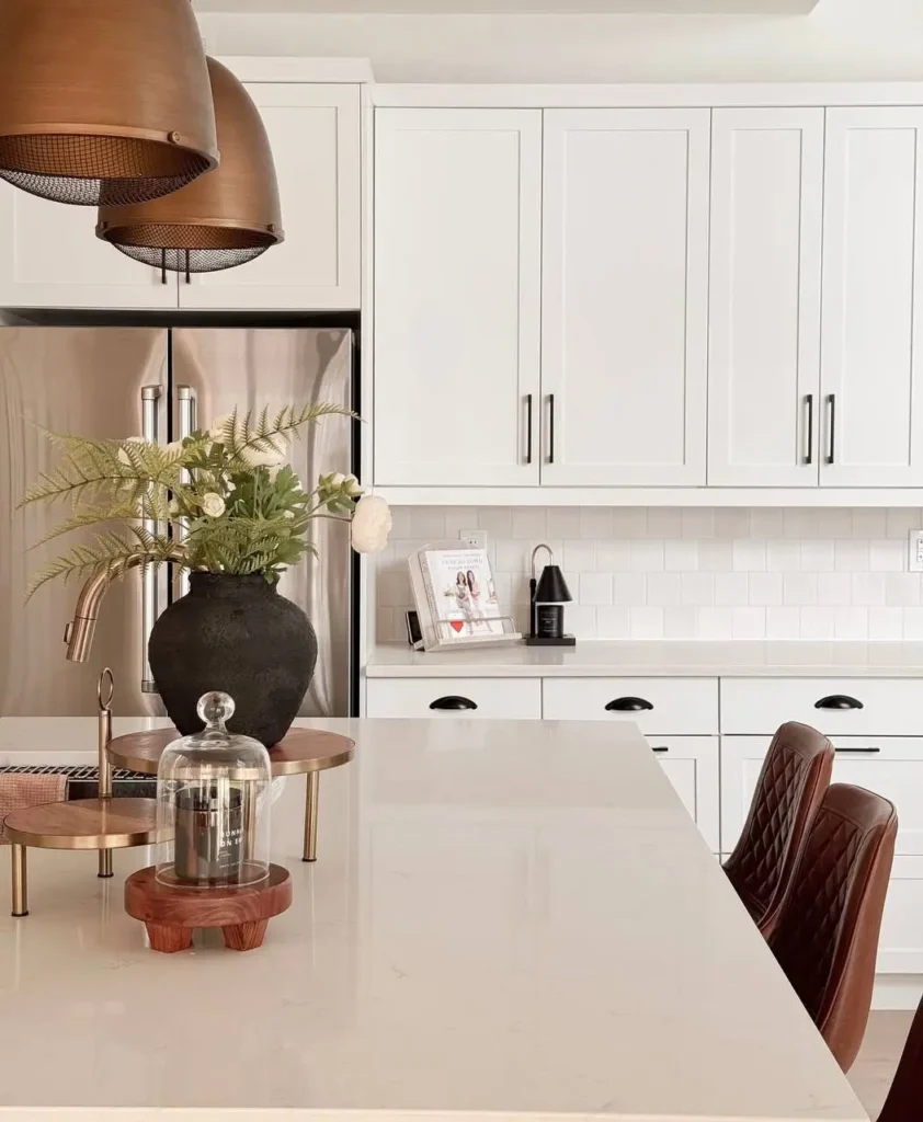 Modern farmhouse kitchen with white shaker cabinets, copper pendant lights, and brown leather stools.