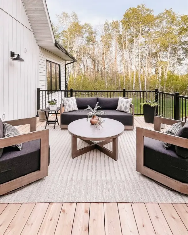 Modern farmhouse deck with gray and wood outdoor furniture and a textured rug.