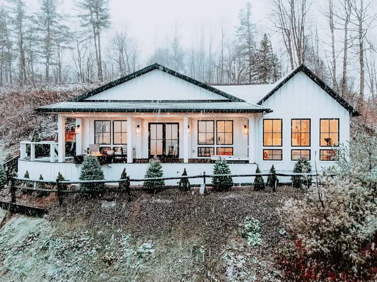 A stunning house design featuring a modern white farmhouse with black trim during a light snowfall.