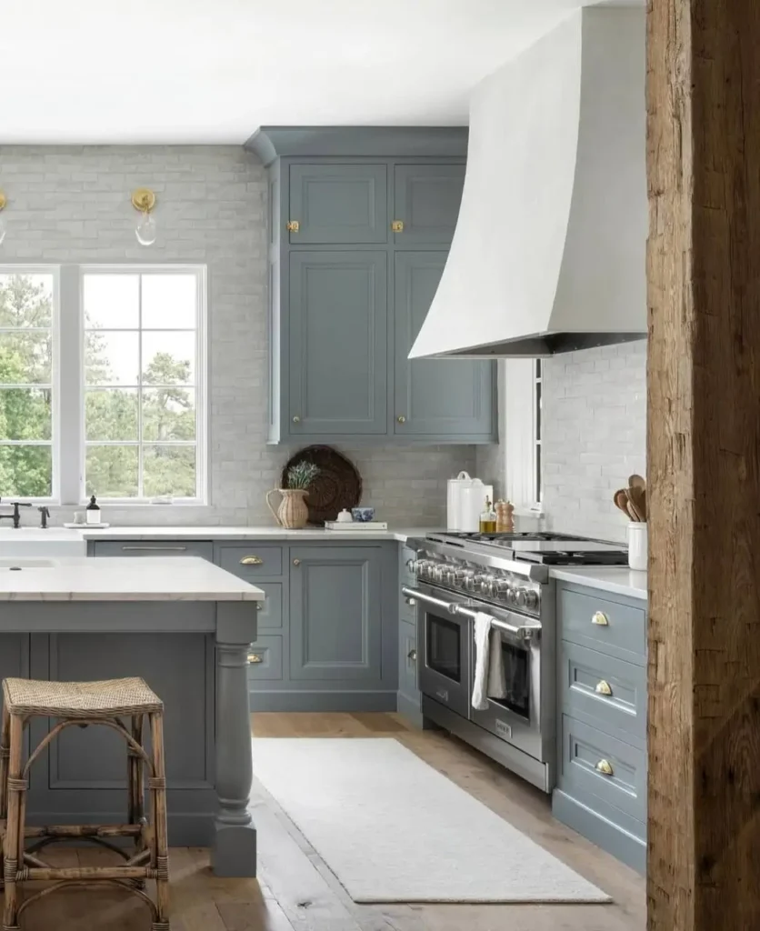 Modern farmhouse kitchen featuring muted blue cabinets, a white plaster range hood, and a large rustic wood beam.