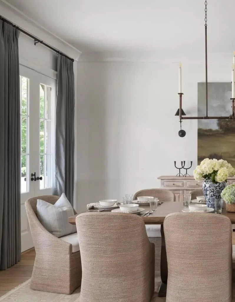 Modern farmhouse dining room with textured woven chairs, a simple metal chandelier, and charcoal gray curtains.