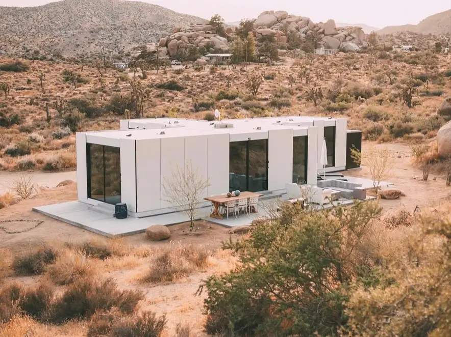 A beautiful modern house design with a white modular structure and large glass windows in a desert landscape.