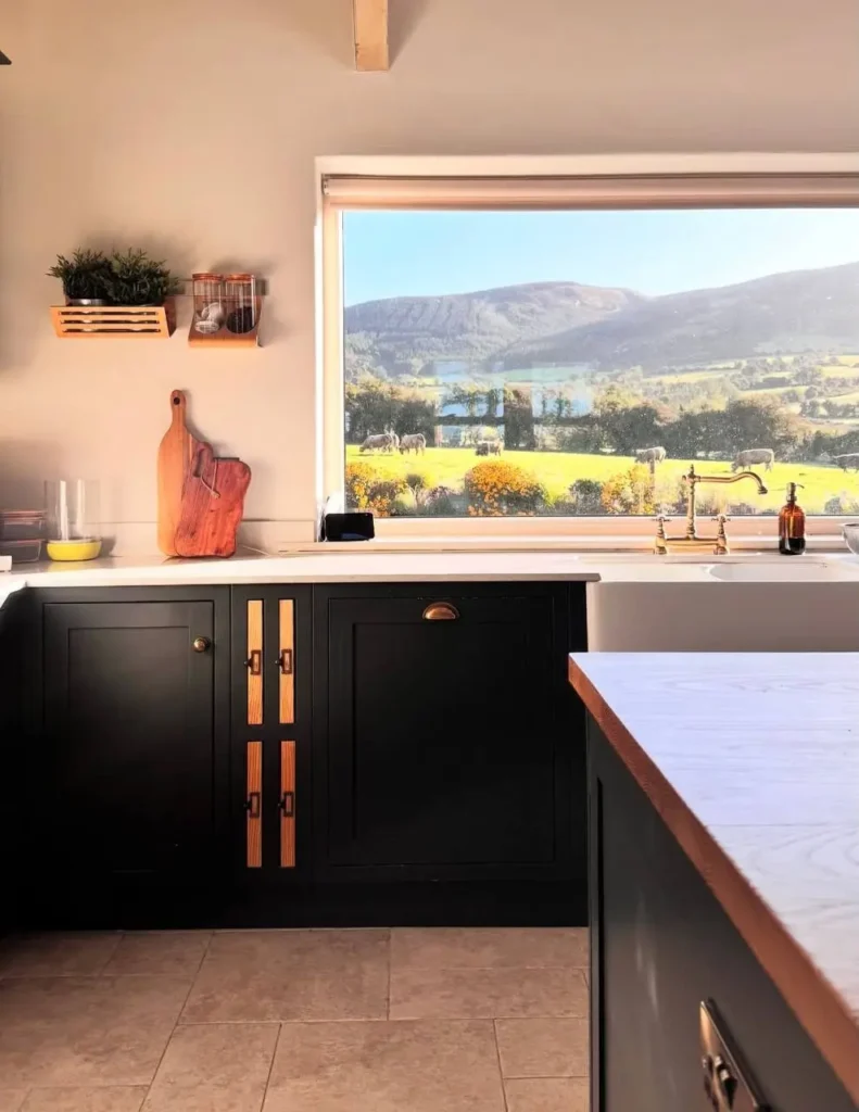 Modern farmhouse kitchen with dark charcoal cabinets, custom wood and metal hardware, and a large window with a scenic view.
