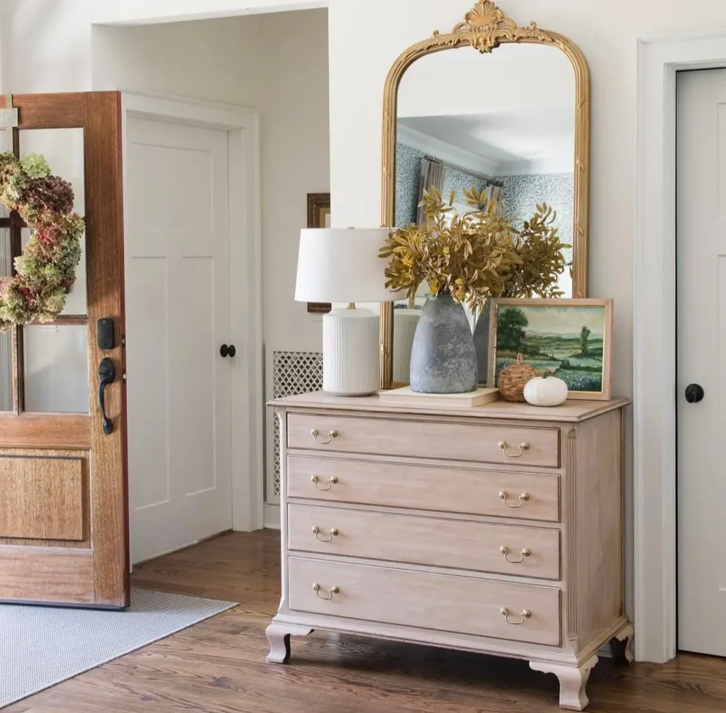 Modern farmhouse entryway with a light wood dresser, large gold arched mirror, and a white modern lamp.