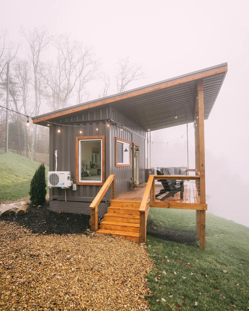 Small gray shipping container home with a covered porch and wooden steps.