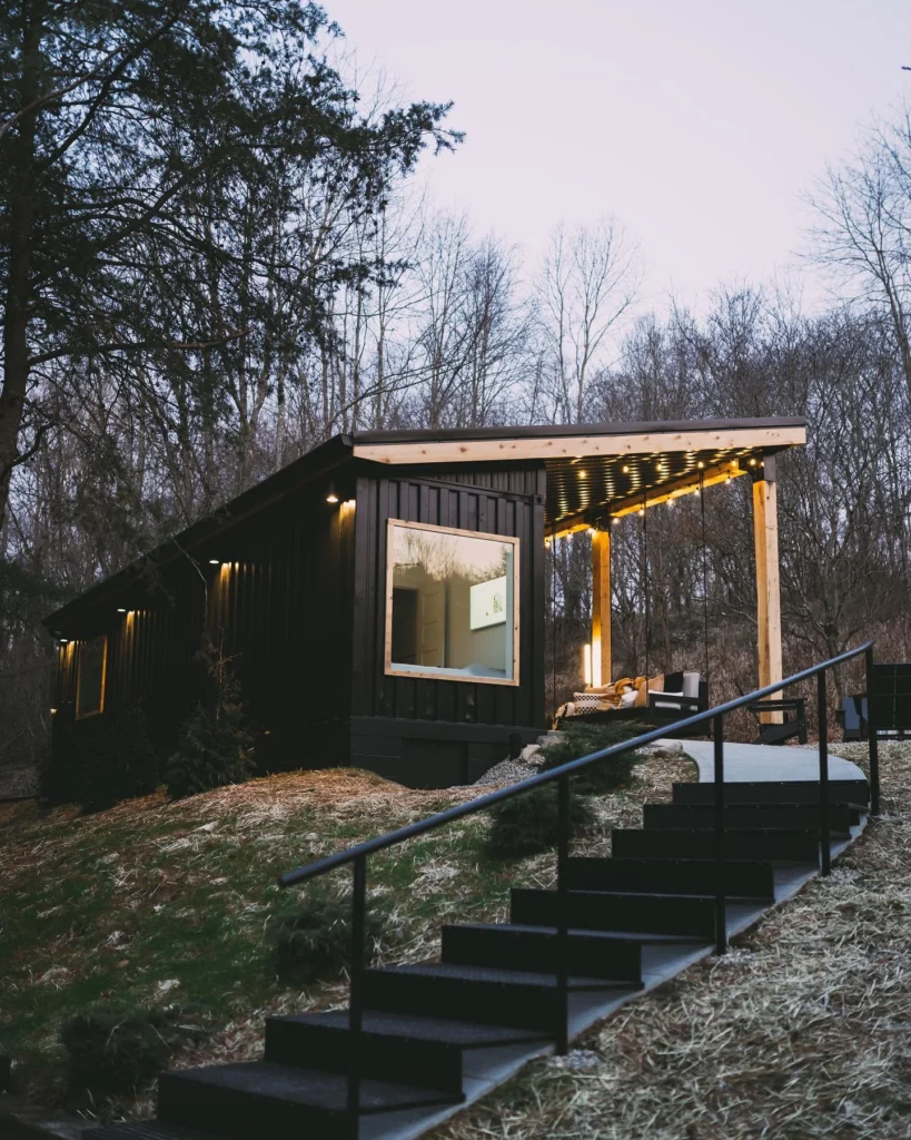 Dark-colored shipping container home built on a hillside with a covered porch.