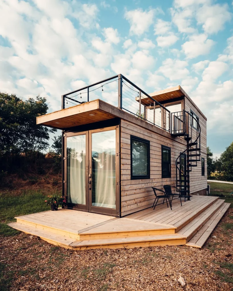 Light-colored shipping container home with multiple decks and a spiral staircase.