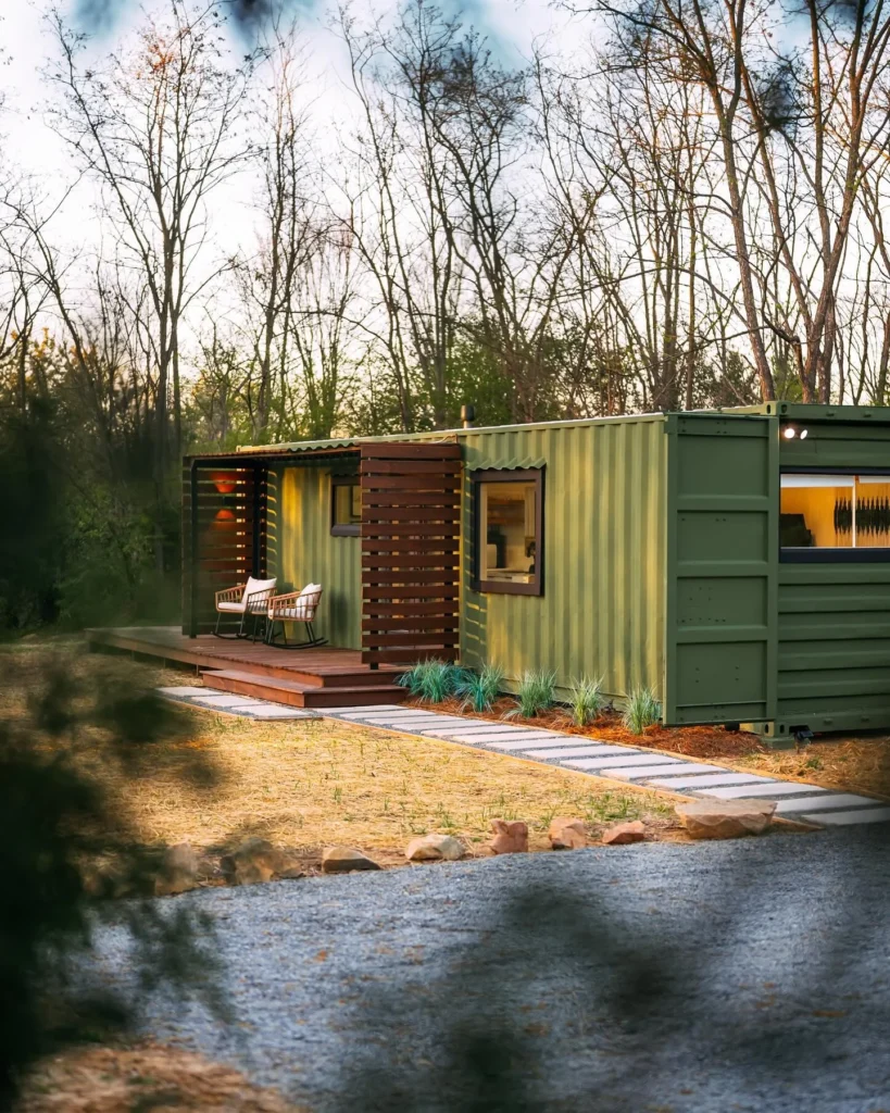 Green shipping container home with wooden deck and slatted privacy screen.