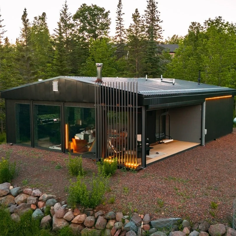 Black shipping container home with large glass windows and an enclosed patio.