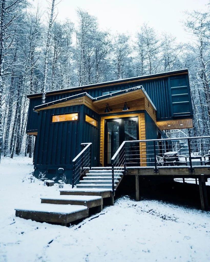 Dark-colored shipping container home with wood accents in a snowy forest setting - Real shipping container homes