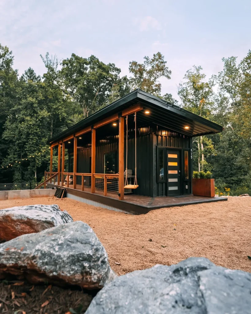 Dark-colored shipping container home with a large covered porch and a porch swing - Real shipping container homes