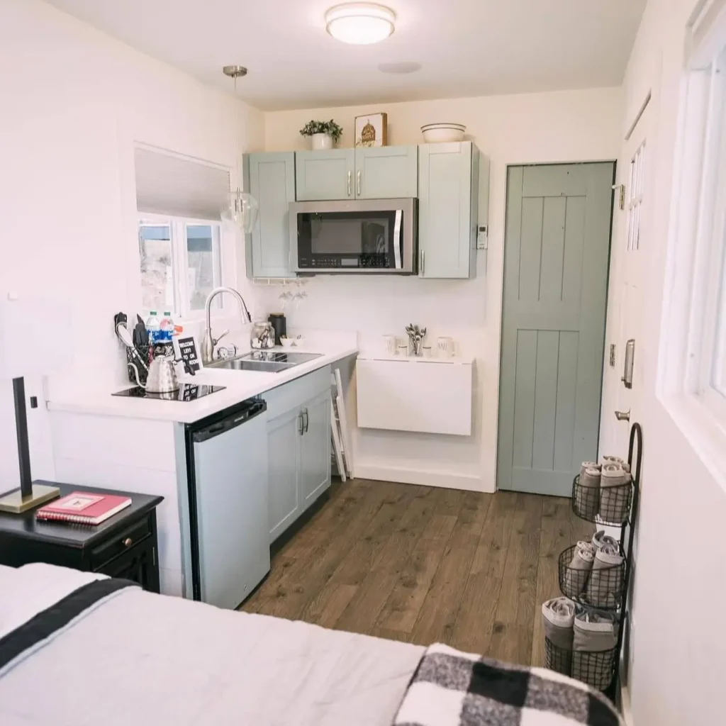 A functional and compact kitchenette inside a tiny container house design, with light green cabinets and a clever fold-down dining table.